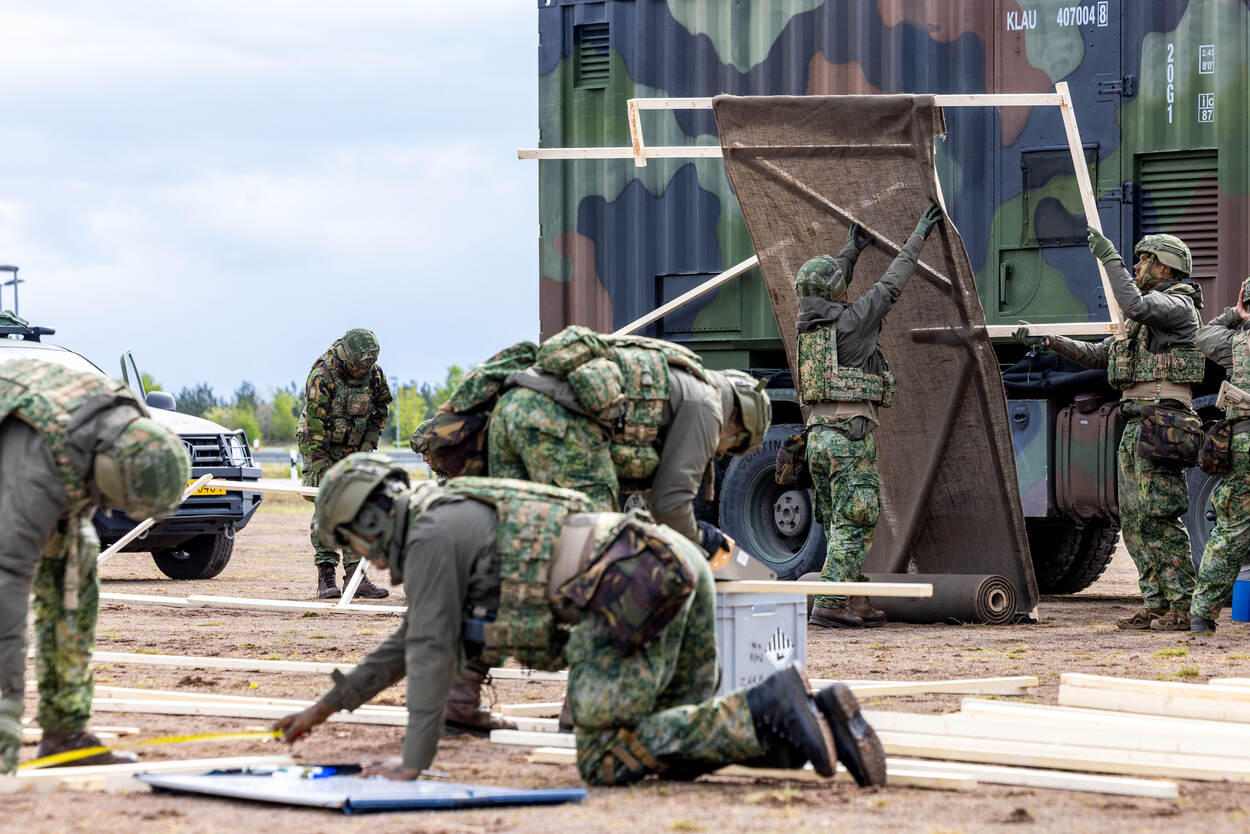 Militairen van 414 CBRN Verdedigingscompagnie bouwen met hamer en zaag in de hand houten constructies. De houten silhouetten bekleden ze met jute.