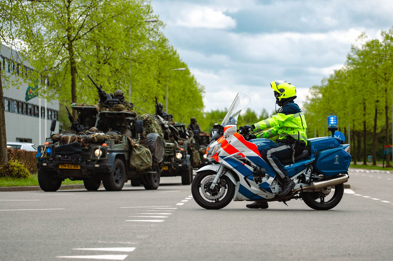 Een motorrijder zet houdt het verkeer tegen zodat een militaire colonne af kan slaan.