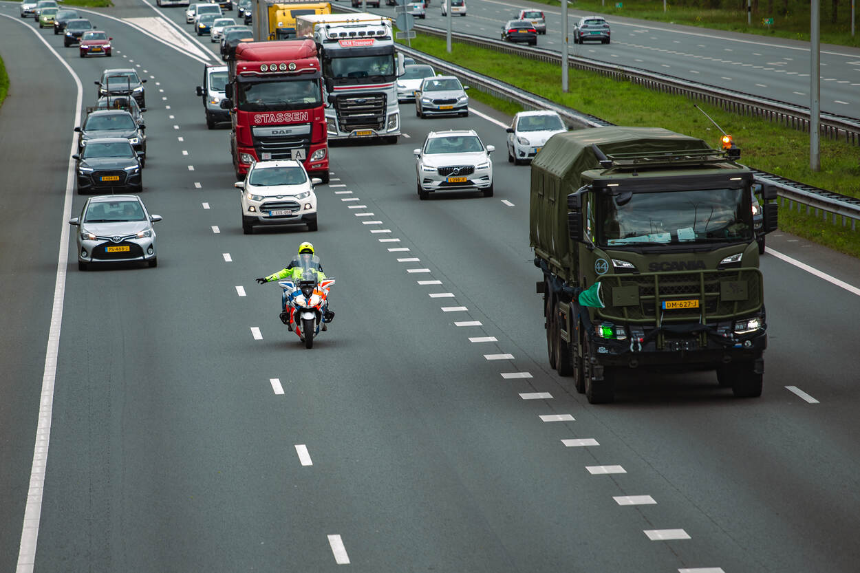 Een motorrijder begeleidt een militaire colonne op de snelweg.