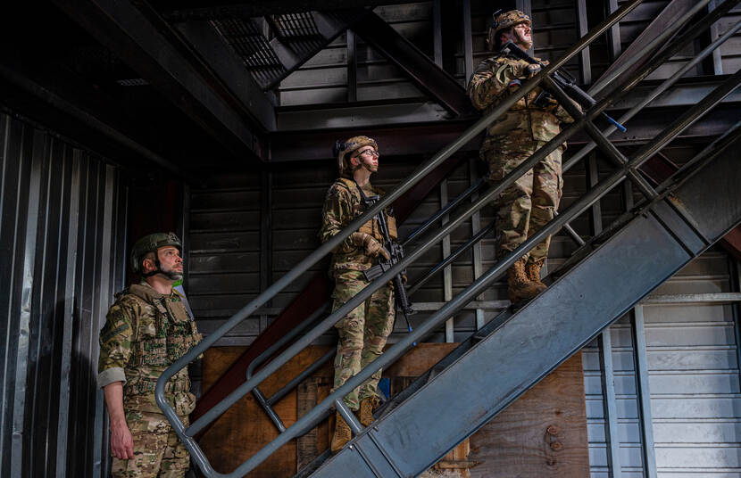 Drie militairen in gevechtspak en met helm en wapen staan op een trap te wachten totdat hun scenario begint.