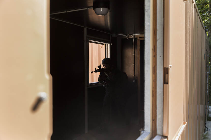 Een militair van 13 Lichte Brigade neemt gewapend zijn positie aan in een raam in een van de oefengebouwen op het militaire oefenterrein in de Marnewaard. Door de schaduw is de militair slechts in contouren te herkennen.