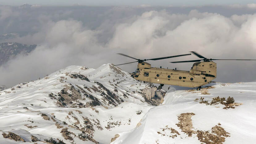 Een Chinook maakt een ridge landing op een besneeuwde bergtop.