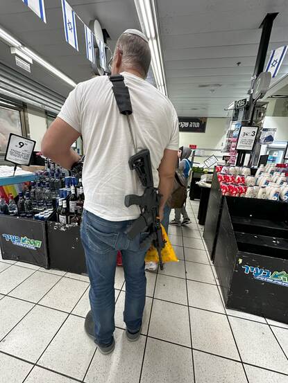 Een Israëlische man in de supermarkt met op z’n rug een lang, zwart wapen.