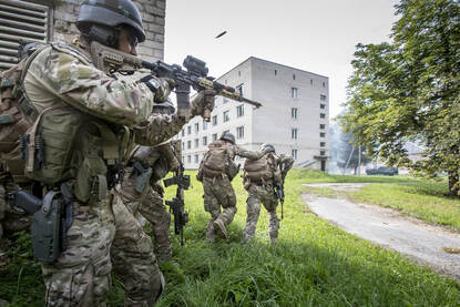 Militairen bewegen al vurend tussen de gebouwen door in het oefengebied van het Litouwse Pabrade.