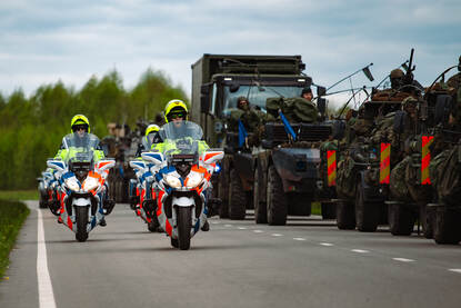 Een groep motorrijders rijdt langs een militaire colonne.