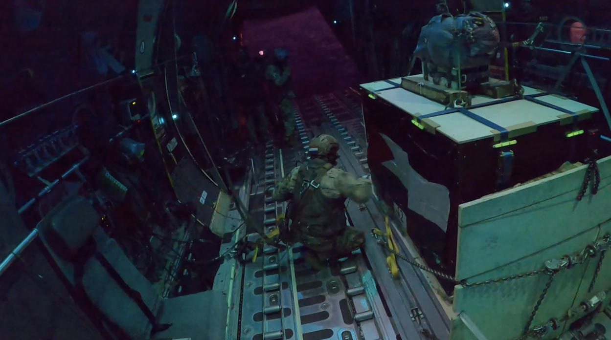 Twee militairen staan in het vliegtuig bij een open laadklep bij de bundels die bijna gedropt gaan worden.