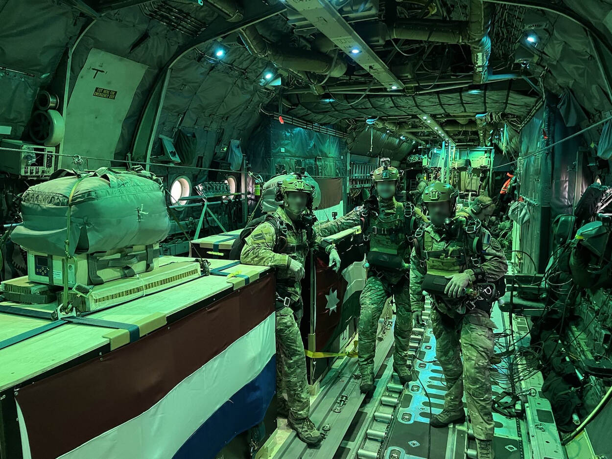 Drie militairen poseren met de bundels met hulpgoederen in het C-130 transportvliegtuig.