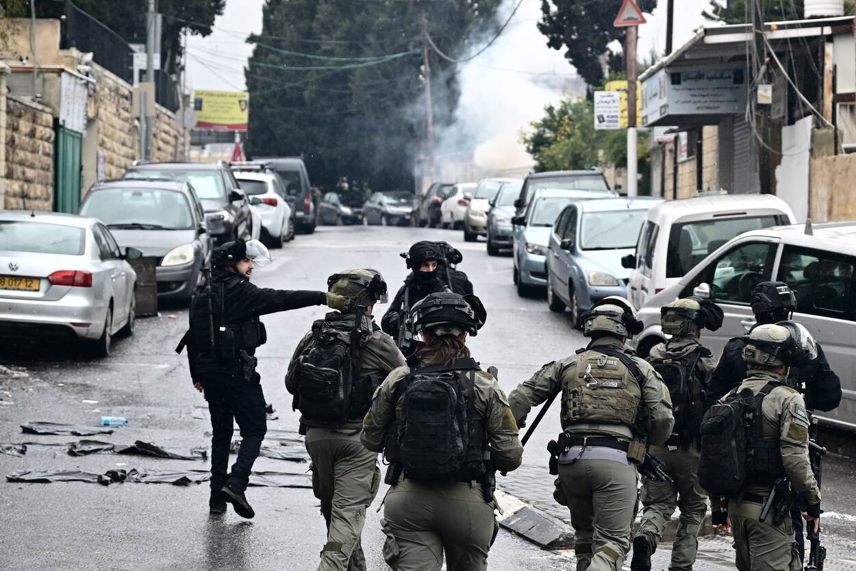 Een straat in Jeruzalem met op de voorgrond Israëlische veiligheidstroepen en op de achtergrond een dikke, gitzwarte rookwolk.