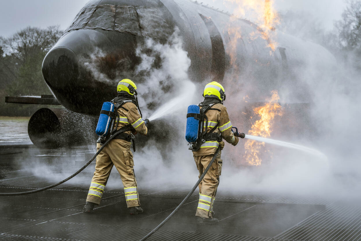 Twee brandweerlieden spuiten omringt door witte rook met een brandslang water op de mock-up.