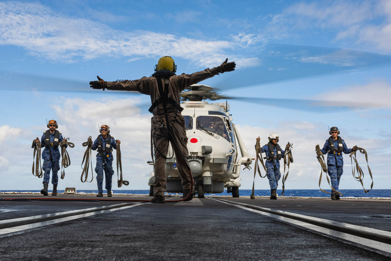 Na landing op het dek van het schip verlaat de bemanning de helikopter en loopt richting de vliegdekofficier.