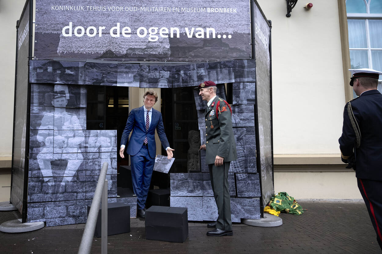 Minister Brekelmans loopt door een foto van een Nederlands-Indisch gezin en opent daarmee de tentoonstelling.