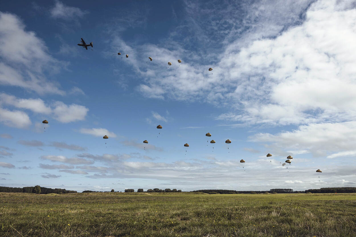 Een vliegtuig laadt parachutisten uit boven een heide.