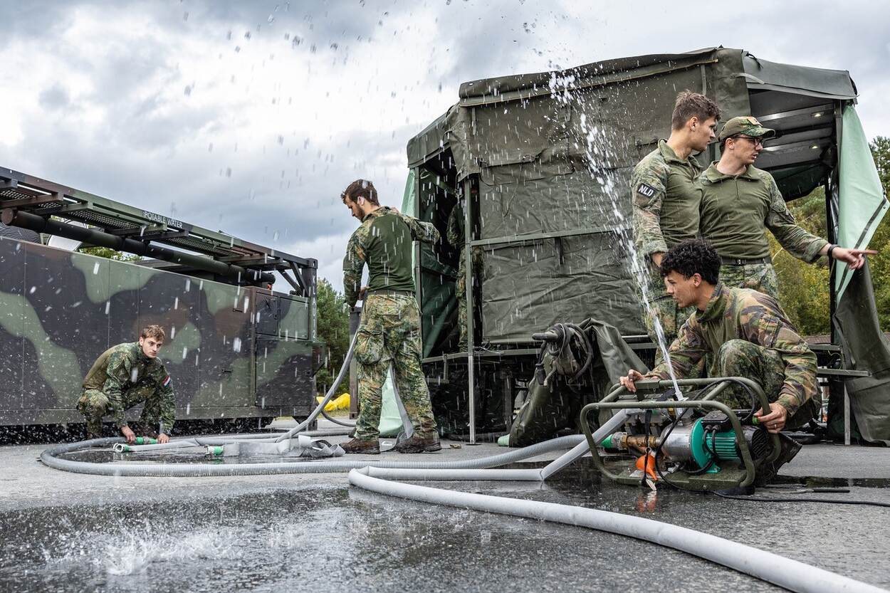 Terwijl het water in het rond spuit voor een test van de mobiele douches, gaan drie militairen verder met het installeren van de wasgelegenheid.