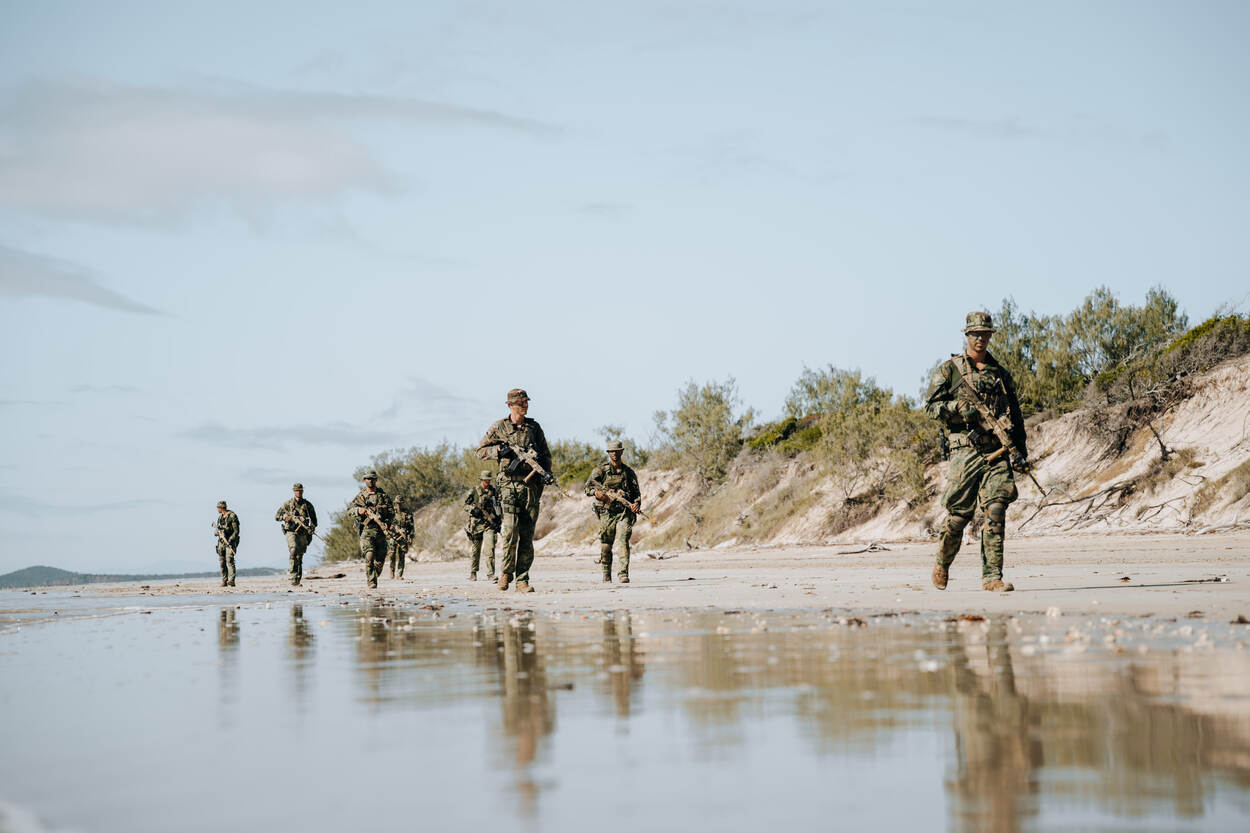 Militairen lopen met een wapen in de hand over een strand.