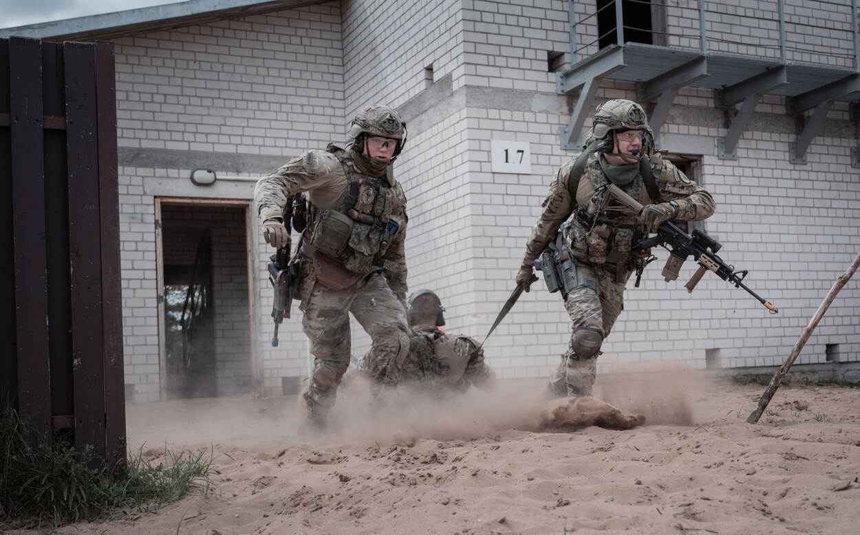 militairen slepen een collega mee door het zand