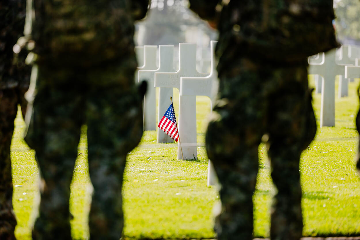 Een witte grafsteen in de vorm van een kruis met daartegenaan een Amerikaans vlaggetje.
