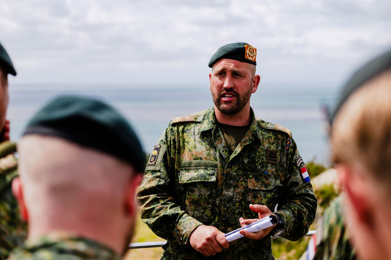 Een militair geeft een presentatie, terwijl hij een opgerold papiertje in zijn handen heeft.