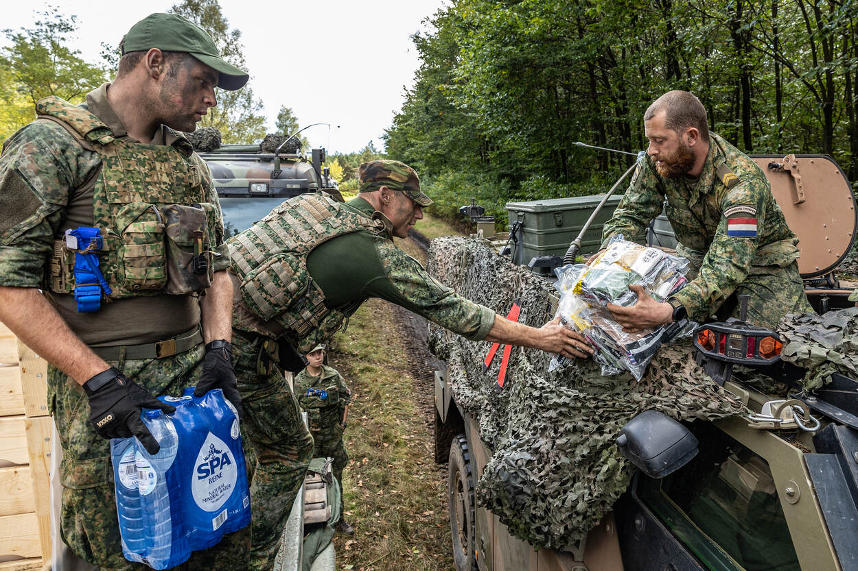 Een militair met een tray bronwater en een militair met een pakket rantsoenen bevoorraden een voertuig van de technische dienst.