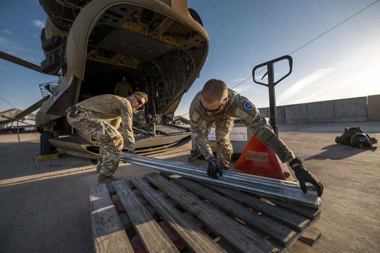 Een doorgunner en een loadmaster brengen metalen buizen aan boord van de helikopter.