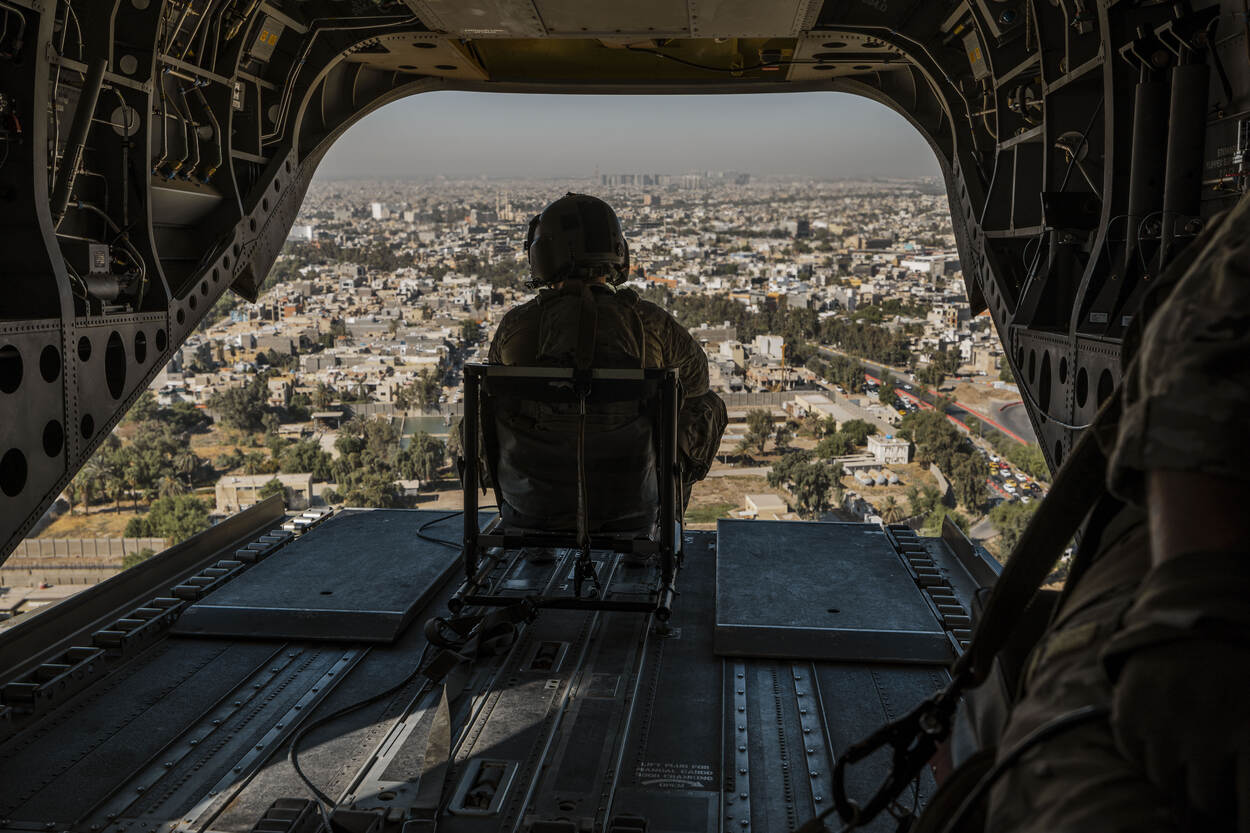 Doorgunner kijkt vanuit de achterkant van de helikopter neer op de stad onder hem.