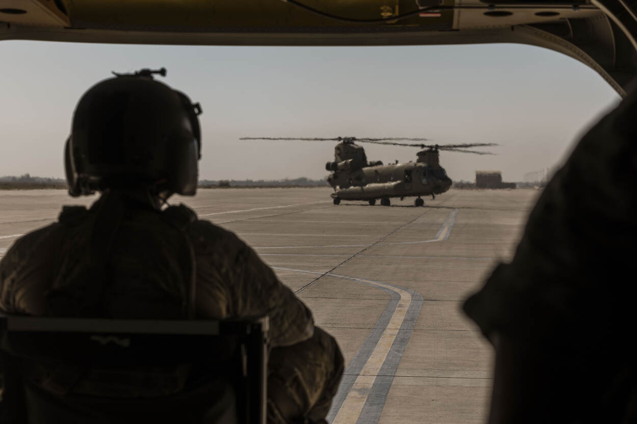 Een doorgunner kijkt vanuit zijn helikopter in de hitte van Irak naar een andere helikopter op de landingsbaan.