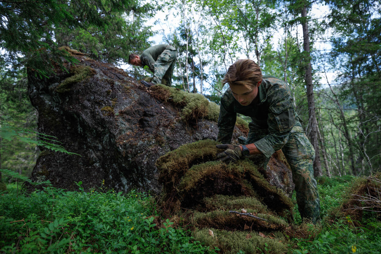 Militair verzamelt mos voor het dak van een onderkomen.