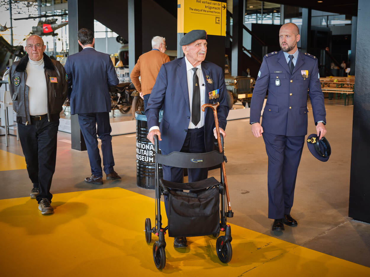 Een postactieve veteraan op leeftijd lopend met een rollator onder begeleiding van een jonge actieve veteraan.