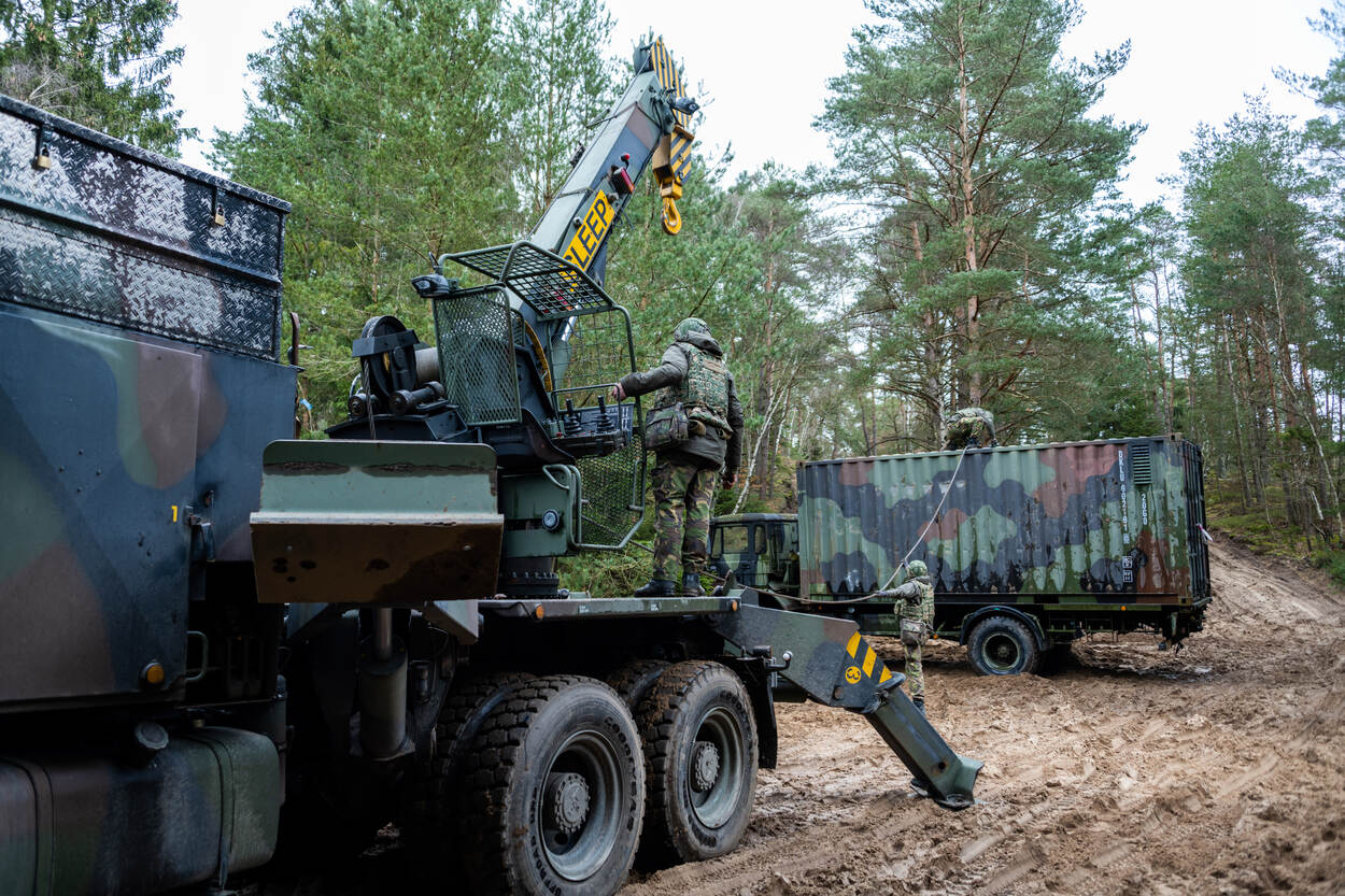 In een bosomgeving trekken militairen met behulp van een bergingsvoertuig een gekantelde militaire vrachtwagen overeind.