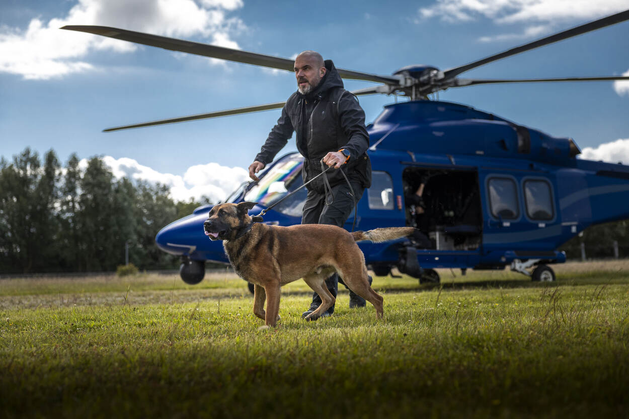 Een marechaussee loopt met zijn hond aangelijnd voor een helikopter langs.