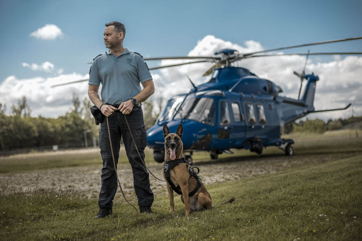 Een marechaussee en zijn hond poseren voor een politiehelikopter.