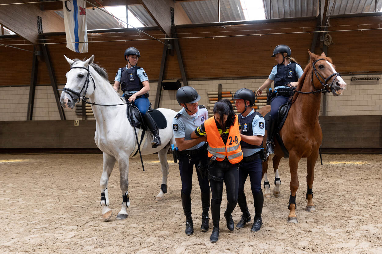 Twee marechaussees te paard begeleiden collega’s tijdens een verplaatsing door een menigte.