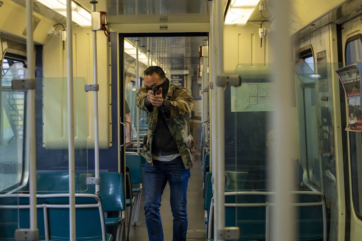 Vermomde man passeert met gesterkte armen en pistool in beide handen een passagier in de metro.