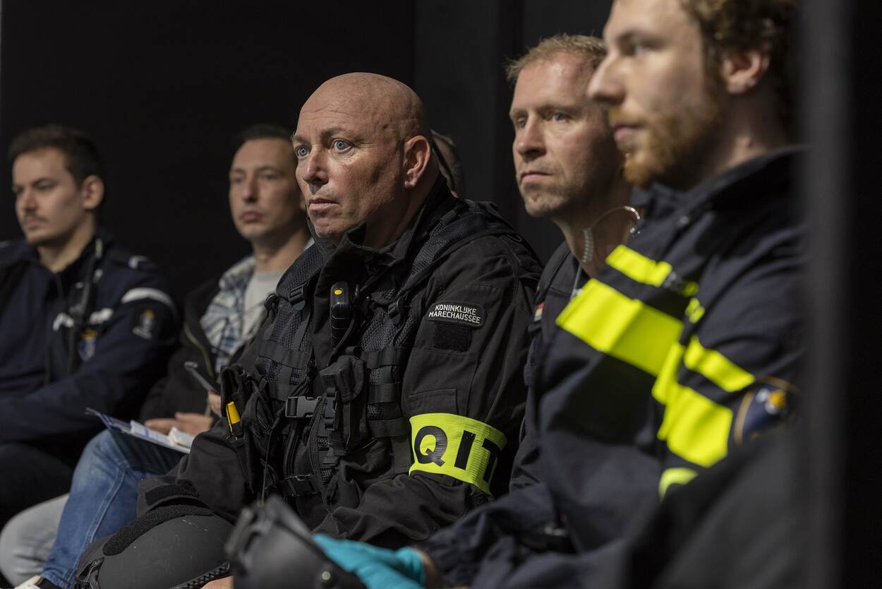 5 mensen zitten op een rij, van wie 4 in uniform en 1 in burgerkleding.