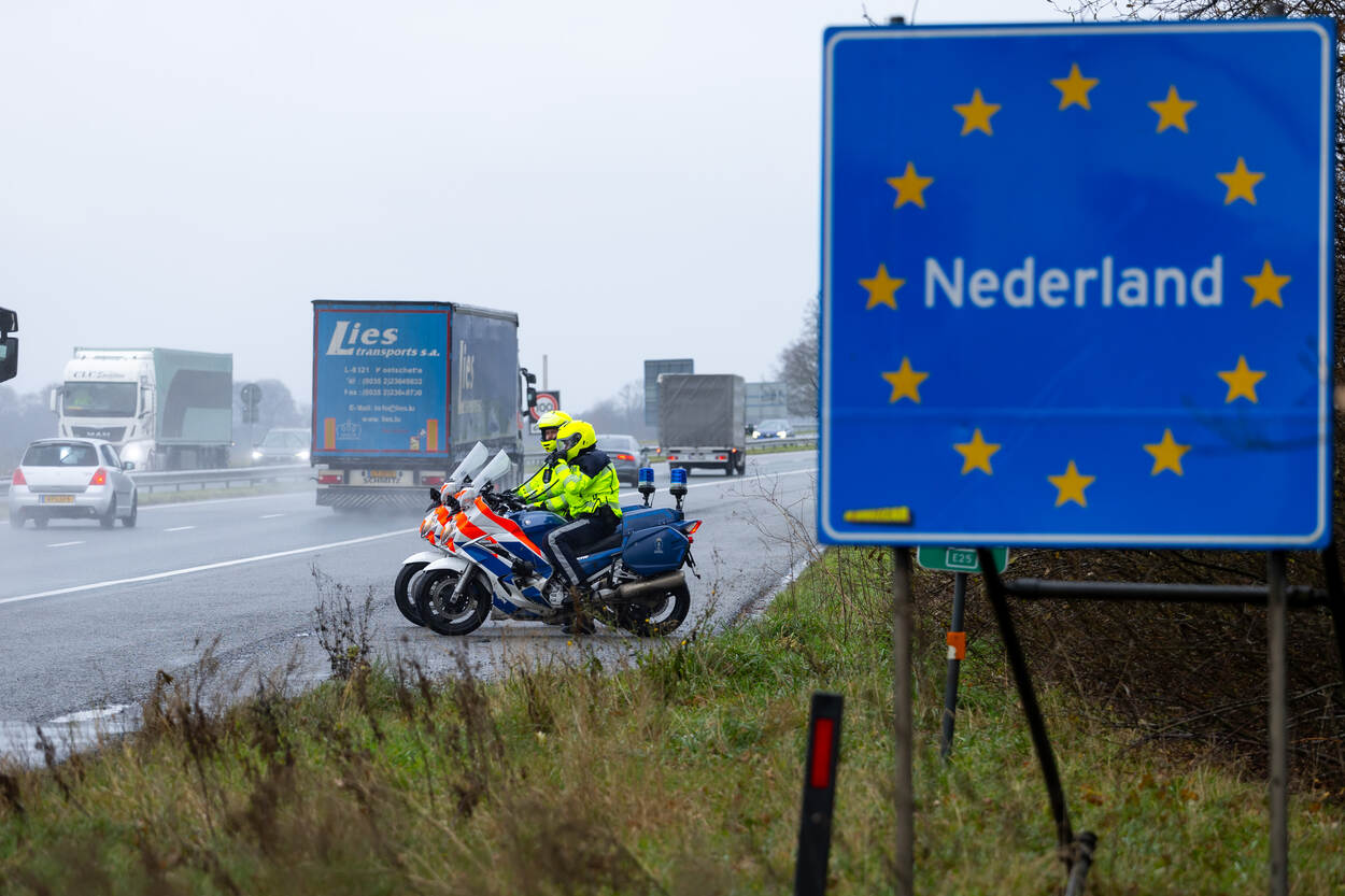 Nederlands grensbord met op de achtergrond marechaussees.