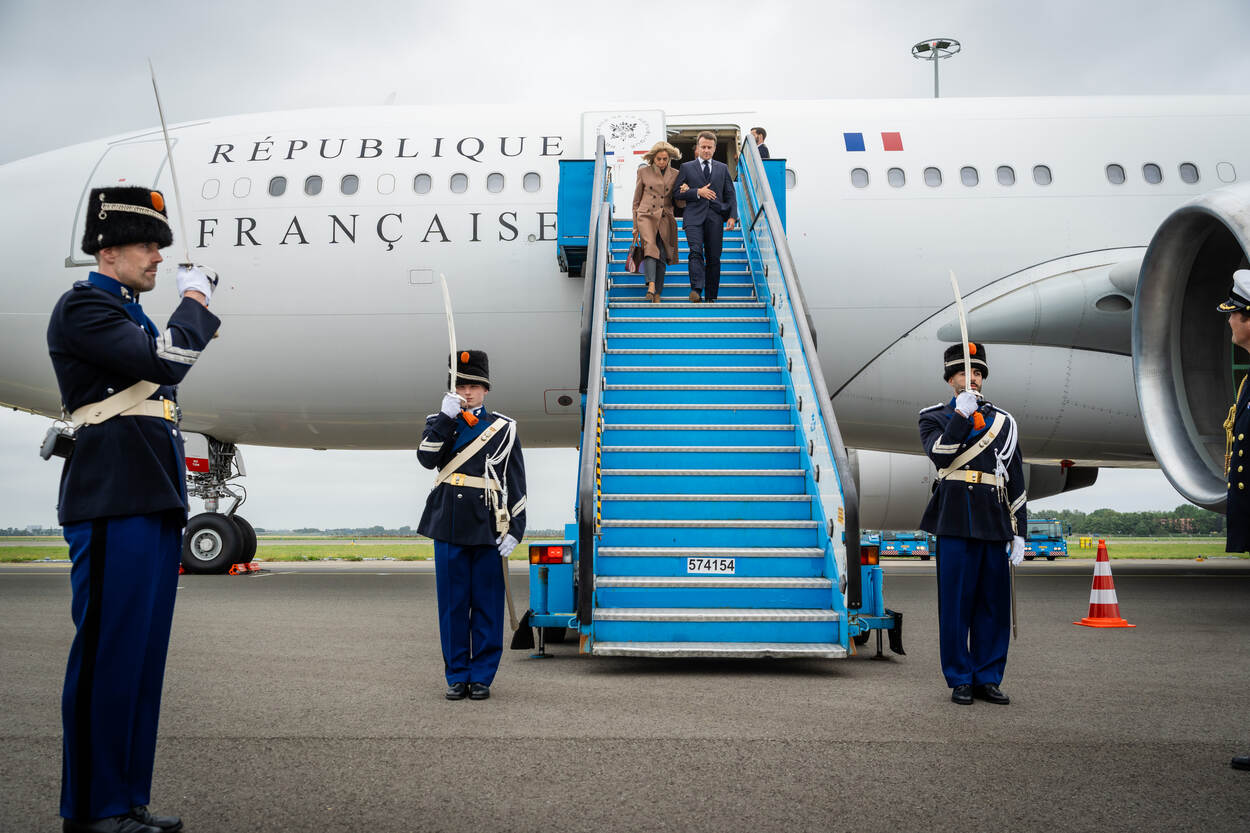 Marechaussees brengen een groet terwijl de Franse president Macron en zijn vrouw van de vliegtuigtrap afdalen.