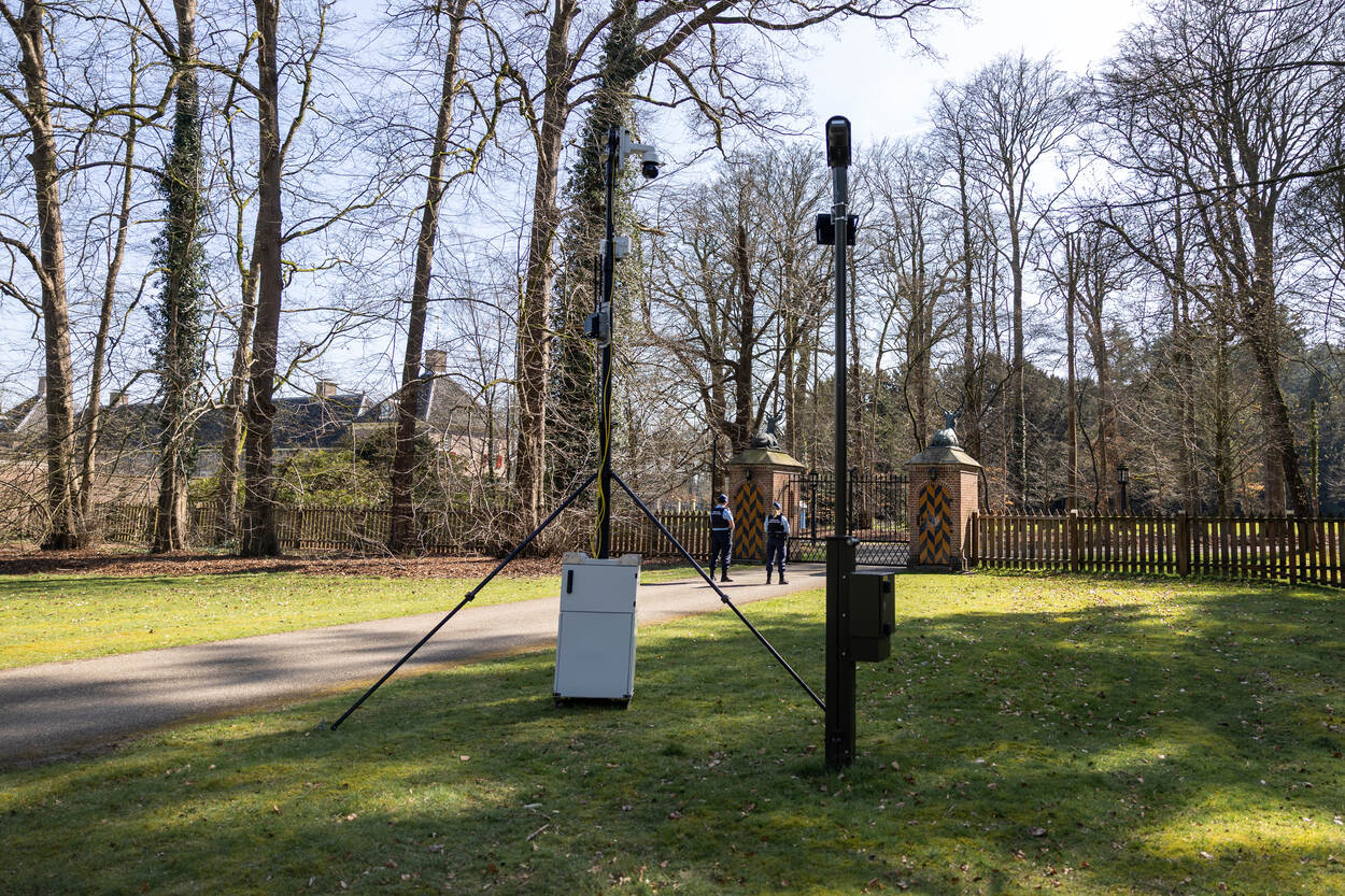 Bomen, takken, hek, 2 leden van de KMar en 2 camera’s op hoogte.