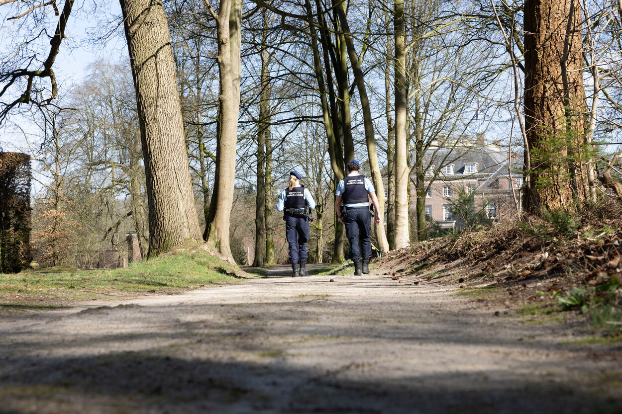 2 marechaussees wandelen door een bos richting een statig gebouw.