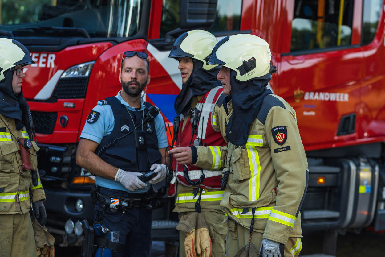 Een marechaussee overlegt met volledig omgehangen brandweermannen.