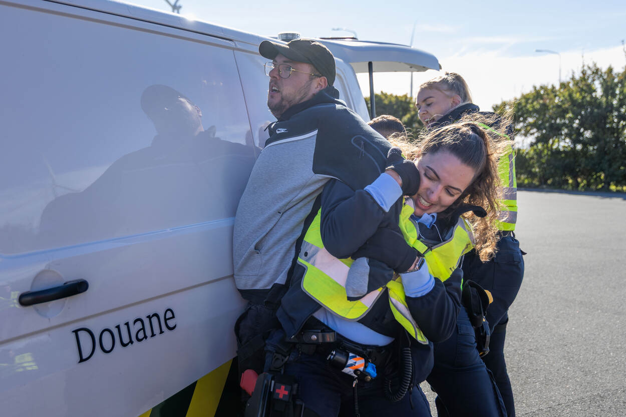 Een verdachte stribbelt tegen en wordt door marechaussees tegen een bus van de Douane geduwd.