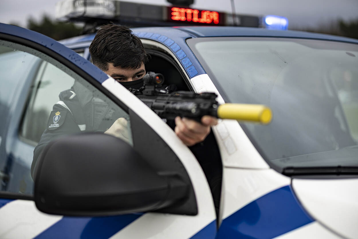 Een marechaussee richt zijn wapen vanachter de deur van zijn auto.