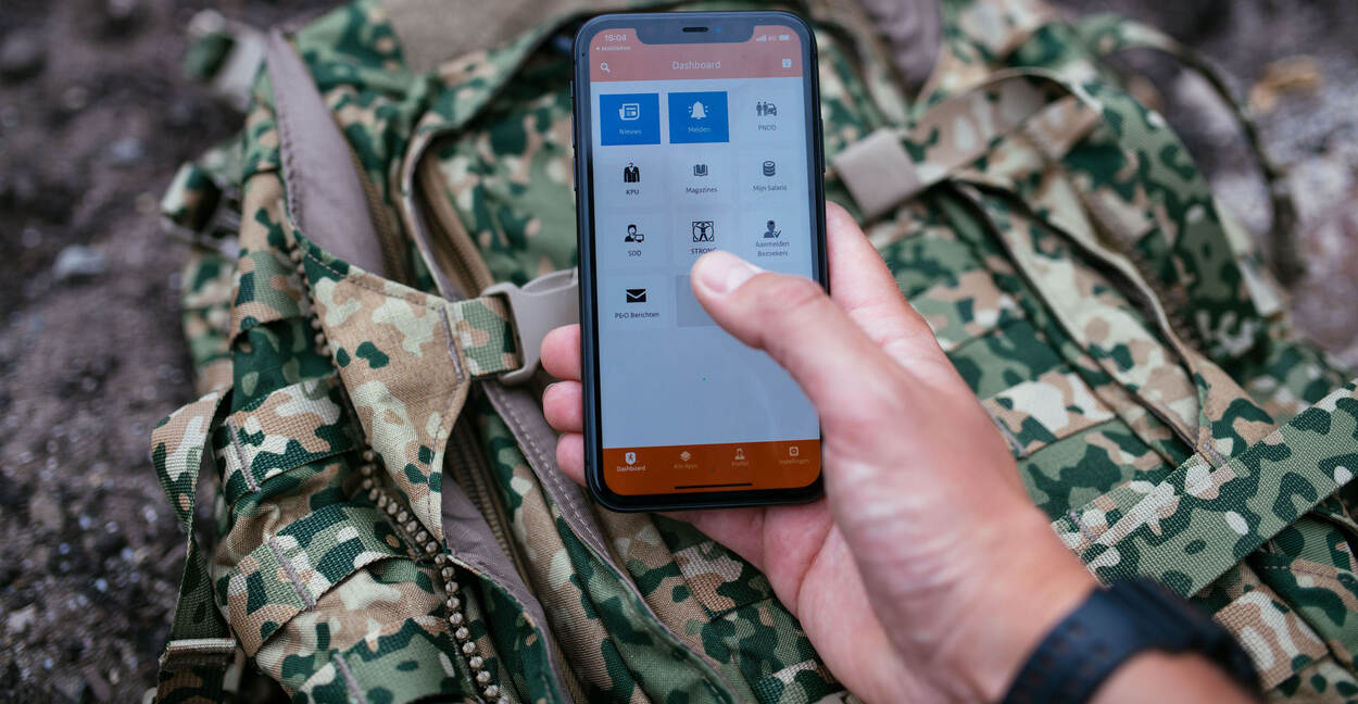 Hand met smartphone met de Mijn Defensie-app op een NFP-rugtas.