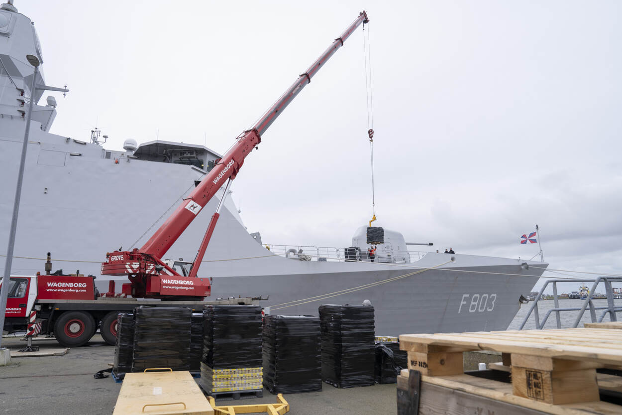 Laden van een marineschip met een kraan en grote kratten.