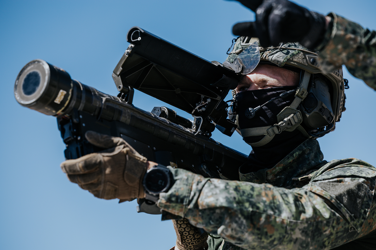 een schutter richt zijn lanceerbuis op een doel. Een instructeur wijst naar het doel.