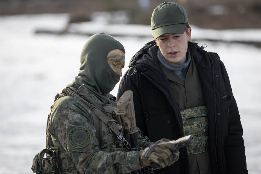 Een fractiemedewerker kijkt naar het pistool van een in camouflagepak gestoken militair.