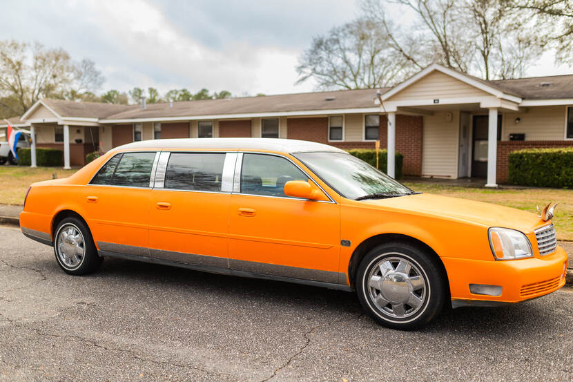 Een felgekleurde oranje limousine met glimmende zilverkleurige velgen, in een straat in Alabama.
