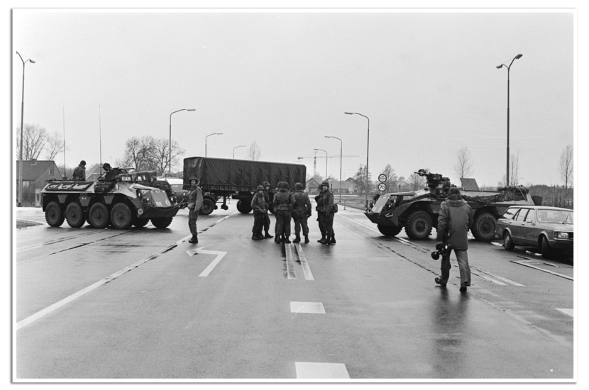 Een weg met links en recht pantserwagens en daartussen een groepje militairen.