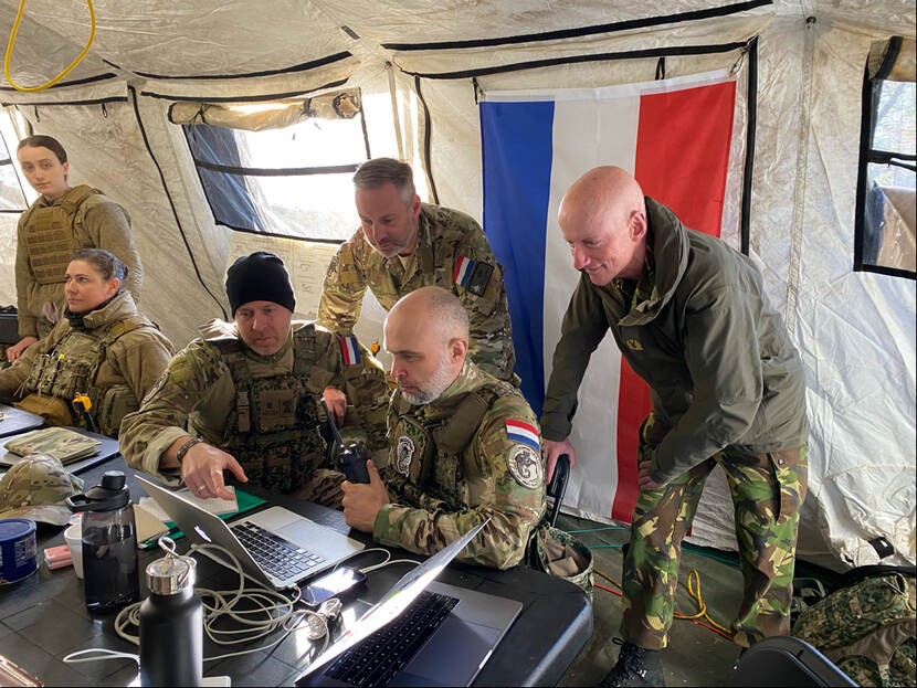 Twee Nederlandse militairen werken in het Joint Operation Center achter een computer en twee Nederlandse collega’s kijken over hun schouder mee.