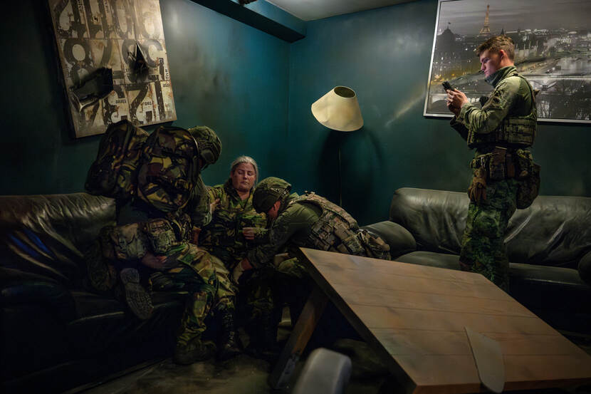 Twee beelden naast elkaar. Op het ene buigen twee militairen zich over het slachtoffer in een van de oefenruimtes te midden van de chaos. Een van hen houdt een naald vast.