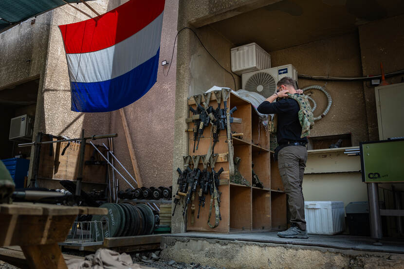 Een militair trekt zijn scherfvest aan in Bagdad. Aan de muur hangt een Nederlandse vlag.