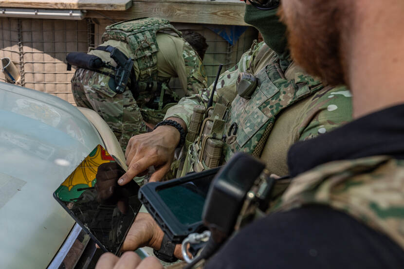 Een militair overlegt met een andere militair, voor het voertuig met de tablet in de hand.